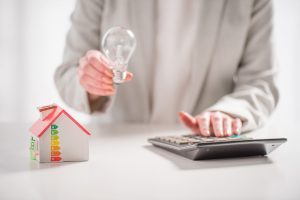 Dame tenant une ampoule calculant à côté d'une figurine de maison