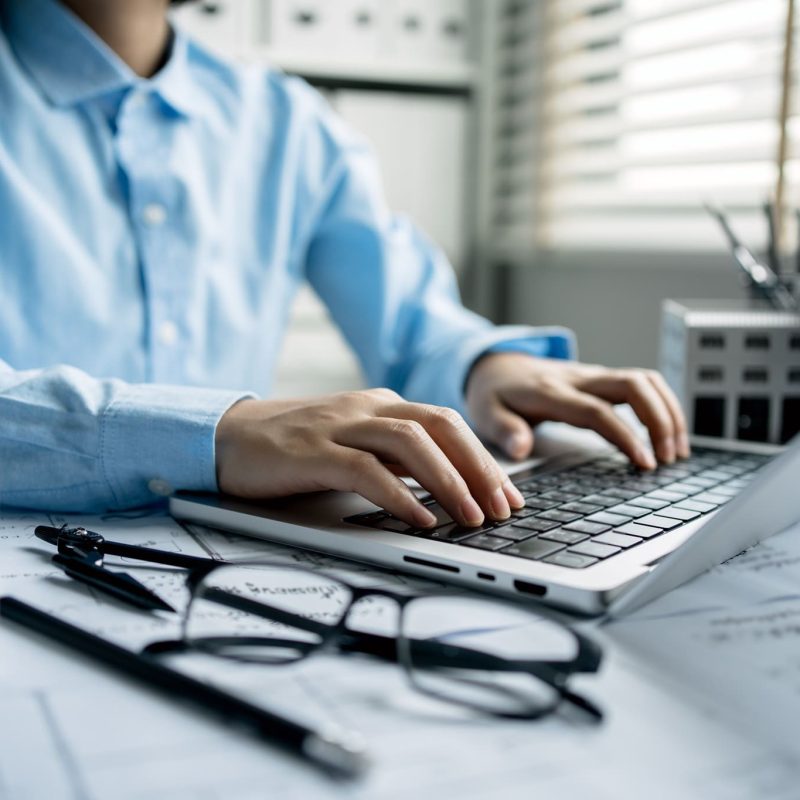 A women architect use laptop and drawing draft on blueprints in the office, working with modern house blueprint floorplans, architectural and construction project concept.